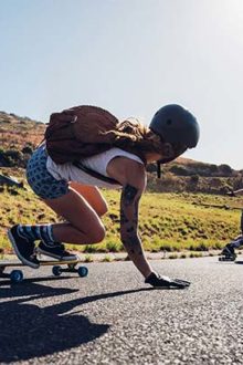 Longboarderin fhärt Longboard und lässt die Hand über den Asphalt schleifen.