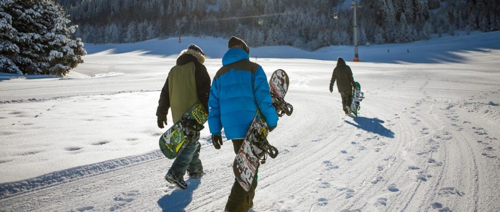 Drei Snowboarde tragen ihr Board zur Piste