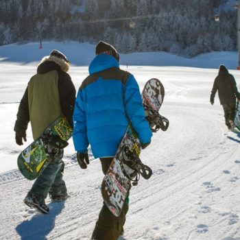 Drei Snowboarde tragen ihr Board zur Piste